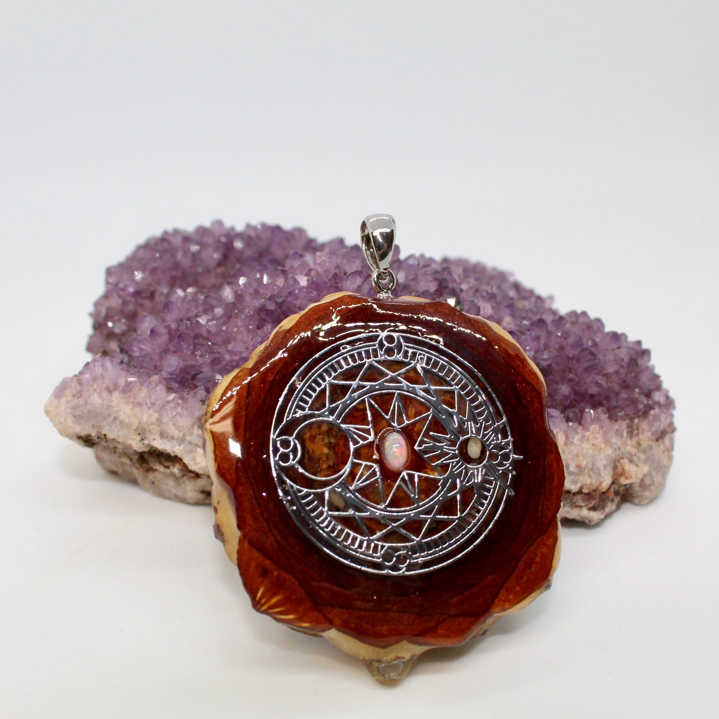 opal pinecone pendant with silver sun and moon symbol displayed on crystal