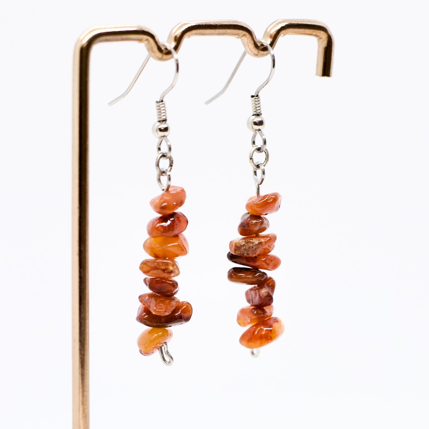close up of Carnelian gemstone dangle earrings on display stand in front of white background