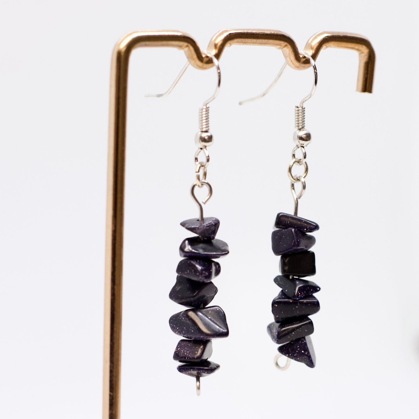 close up of Blue Goldstone gemstone chip dangle earrings on display stand with white background