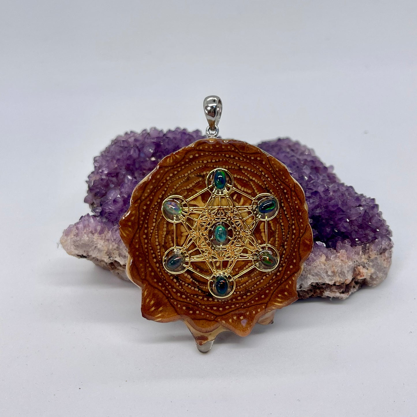 pinecone pendant with black fire opals displayed on Amethyst crystal with white background