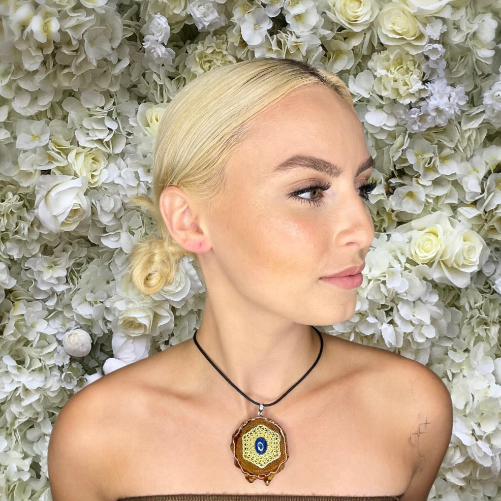 sideview of model wearing pinecone pendant with lapis lazuli stone and gold flower of life symbol