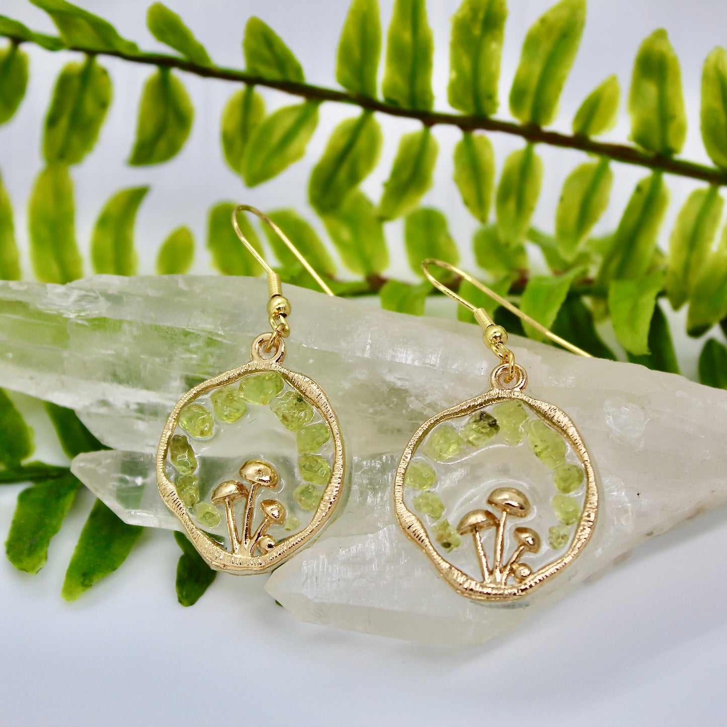 gold mushroom earrings with Peridot gemstone chips displayed on crystal