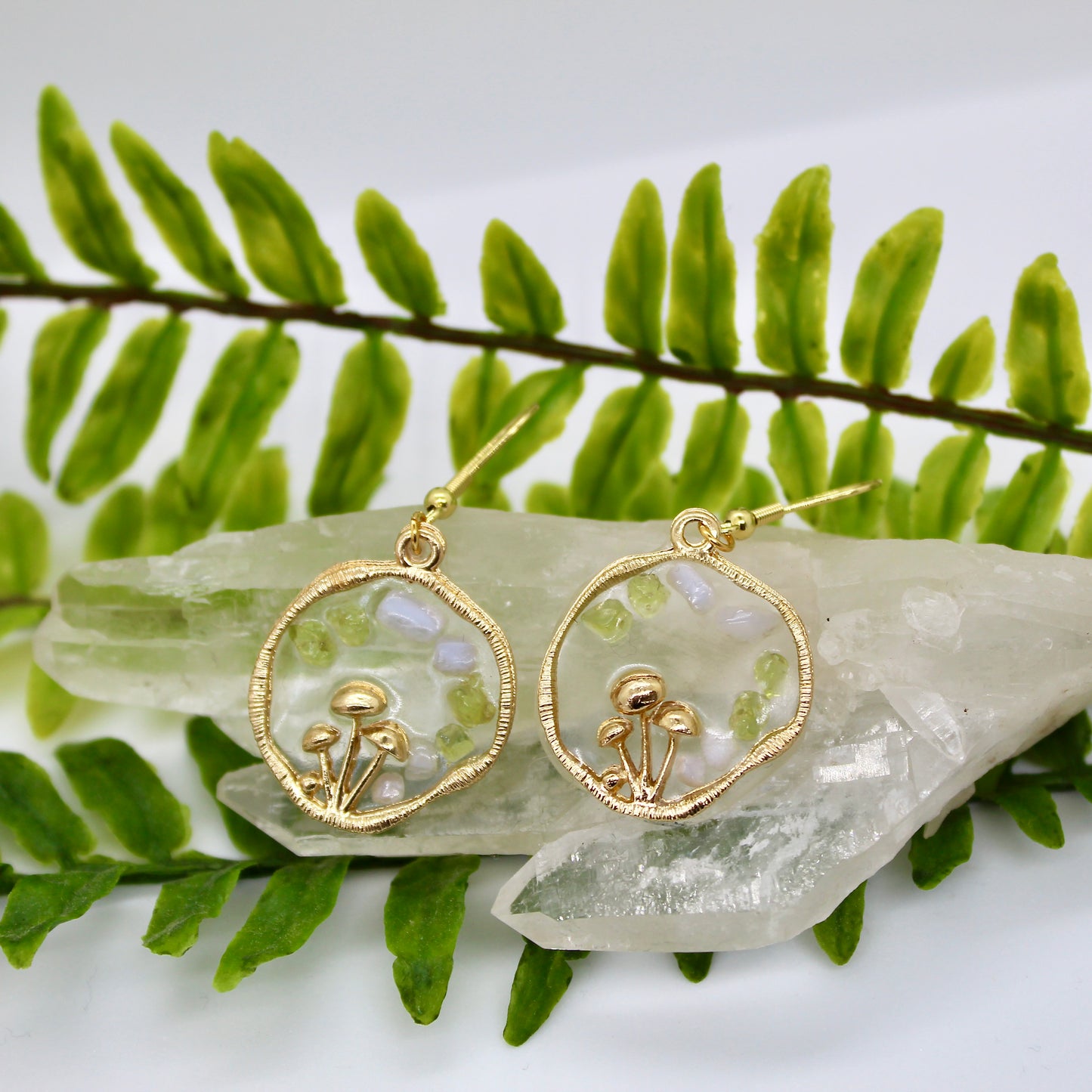 gold mushroom earrings with gemstone chips displayed on crystal 