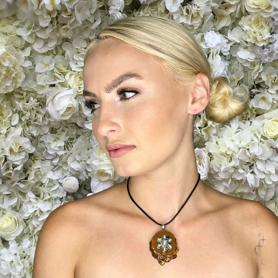 model looking to side wearing pinecone pendant with opals in front of flower background