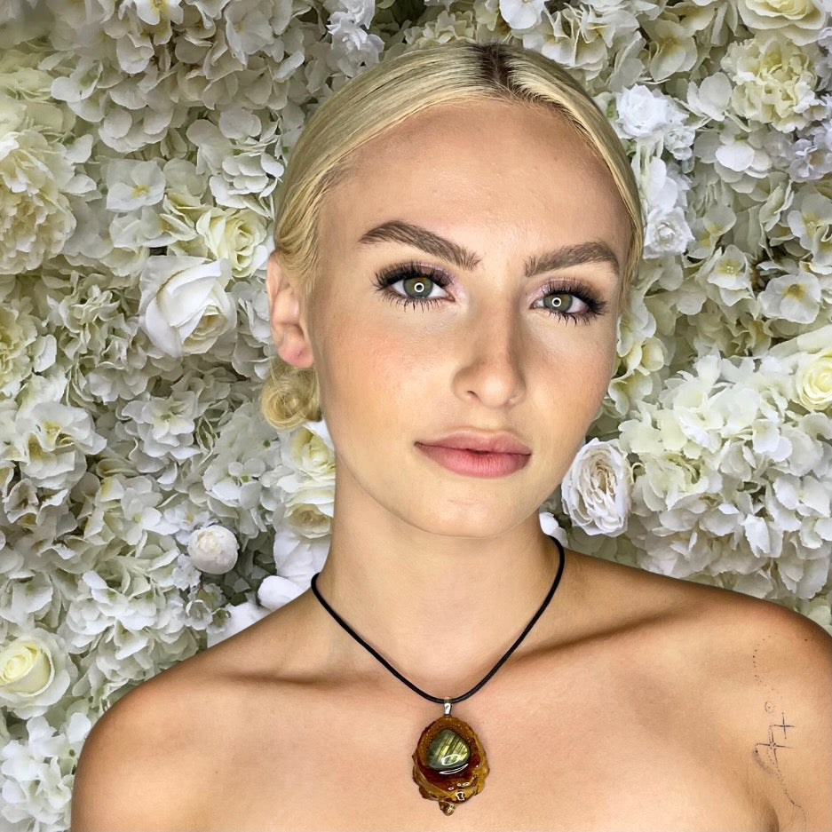 model wearing labradorite pinecone pendant in front of flower background