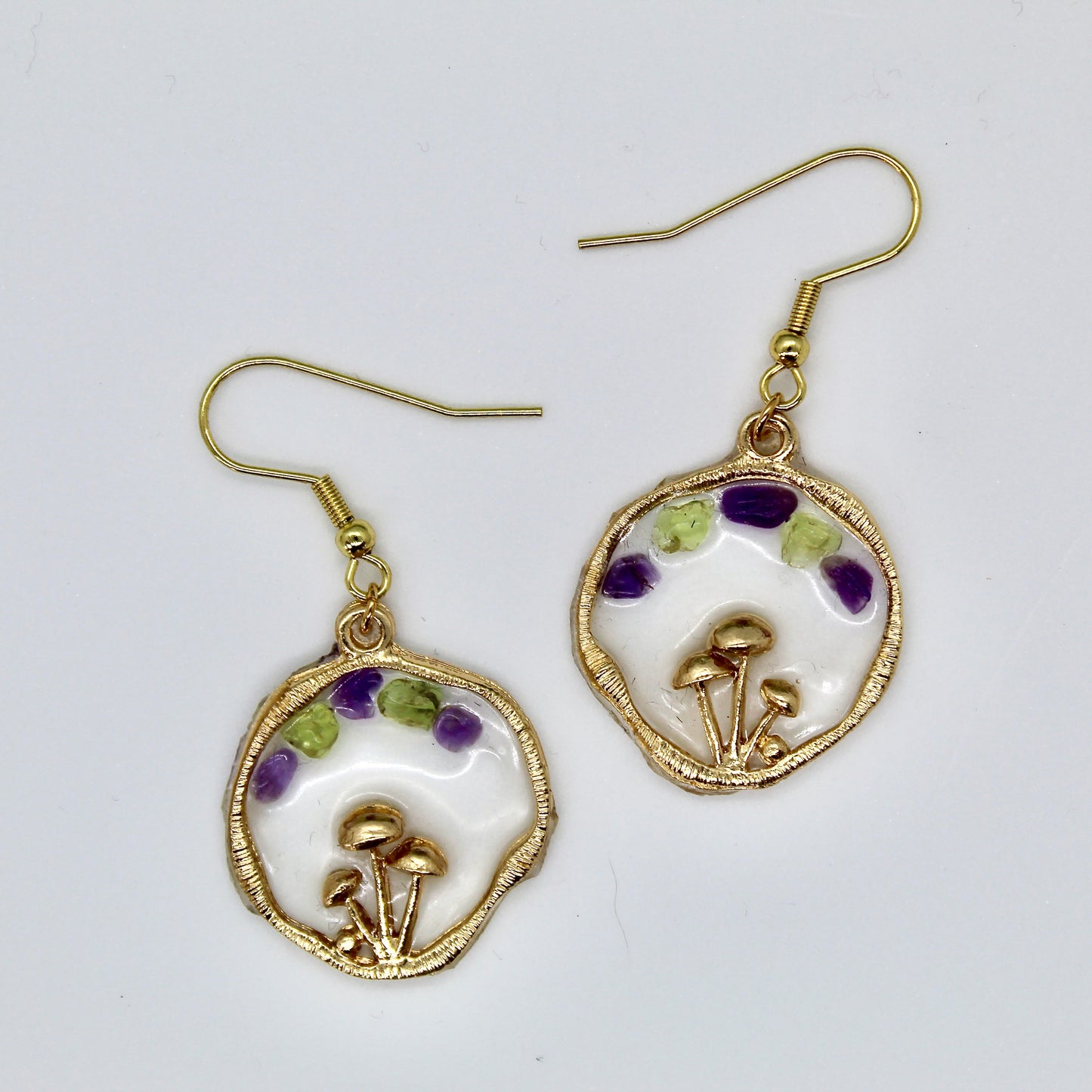 purple and green crystals in gold mushroom earring on white background