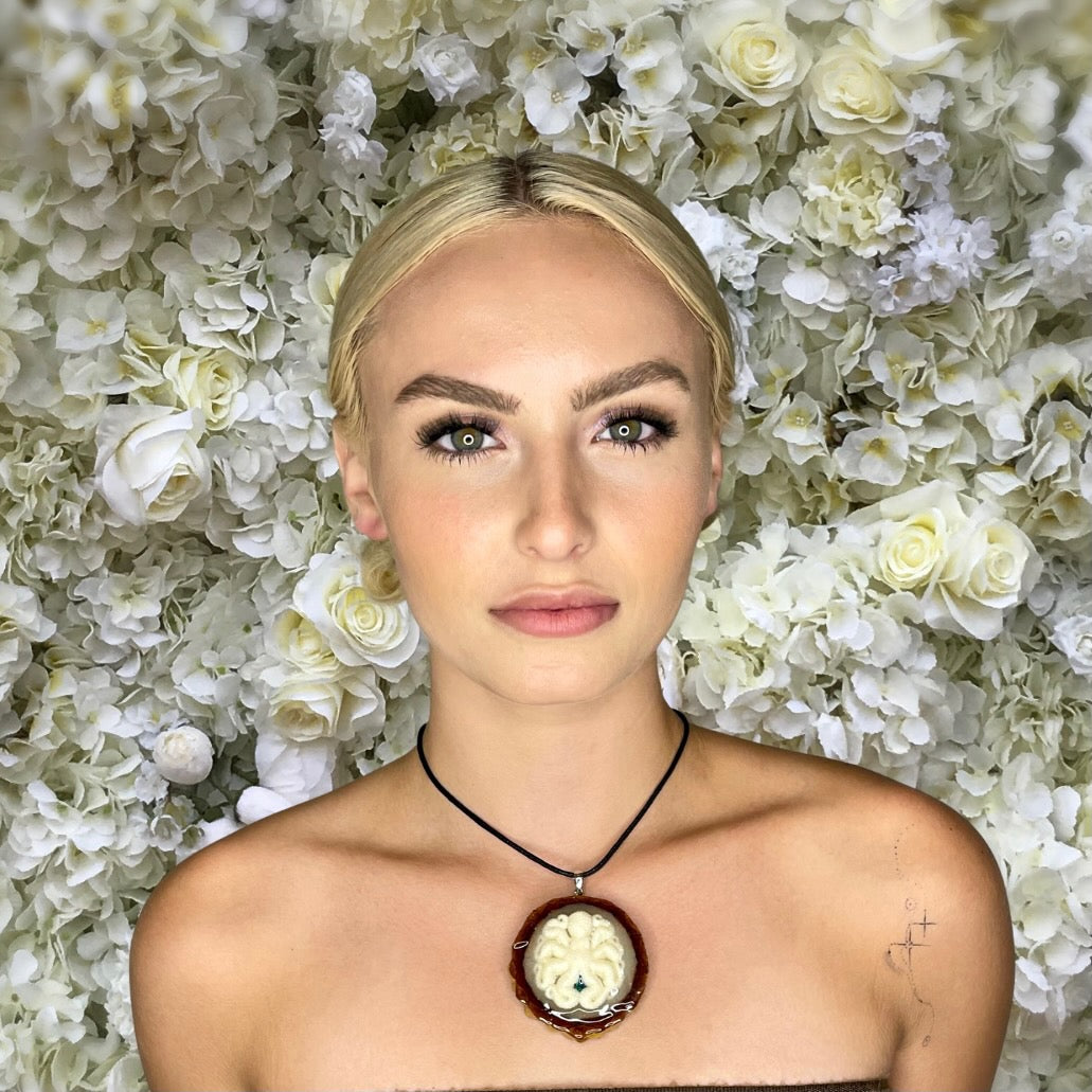 model wearing pinecone pendant with octopus carving in front of flower background 