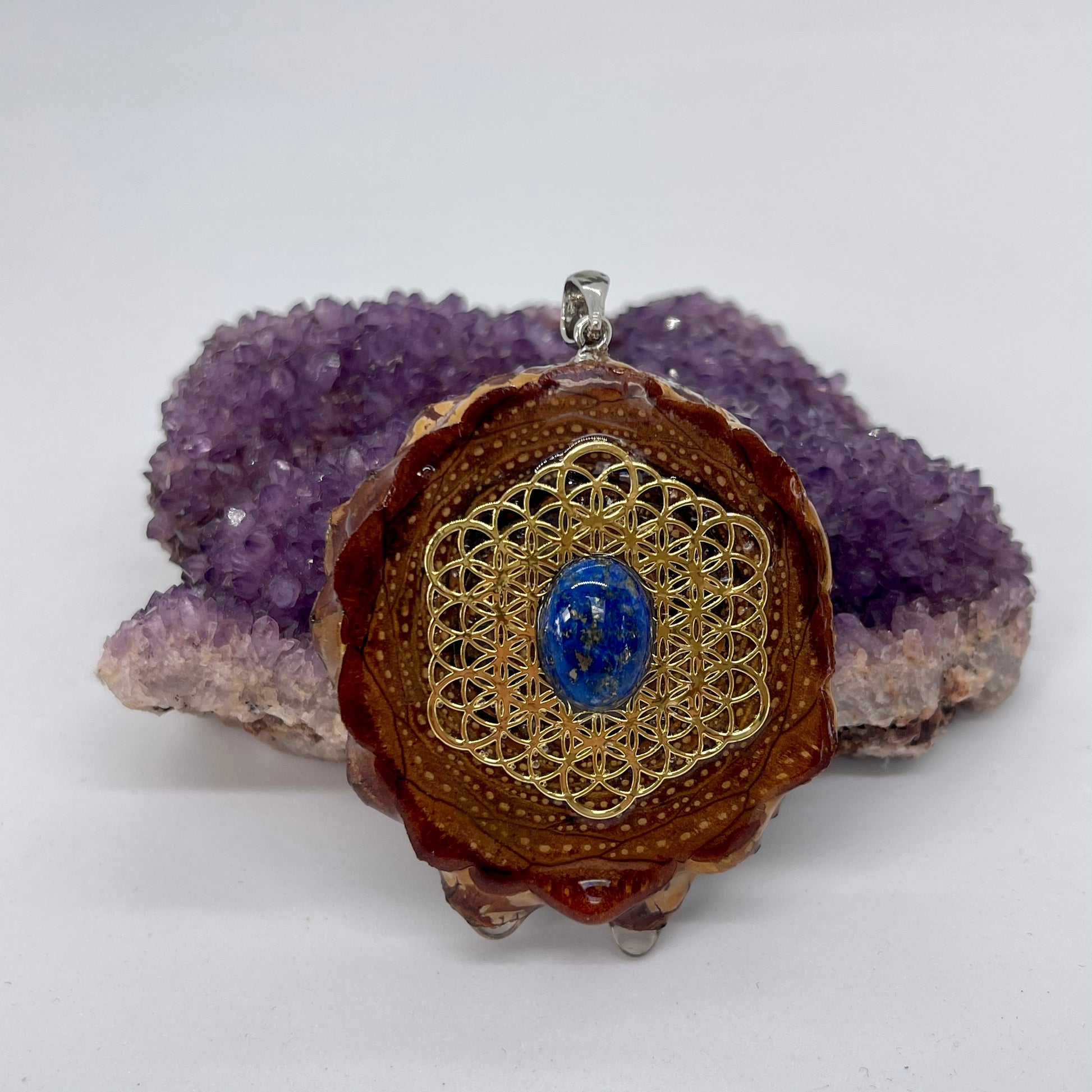 Pinecone pendant with lapis lazuli stone and gold flower of life symbol displayed on crystal 