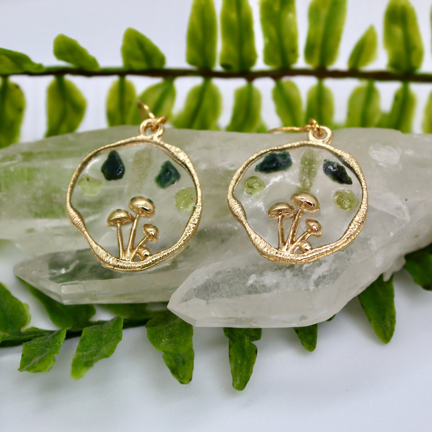 Gold mushroom earrings with peridot and moss agate gemstone displayed on crystal