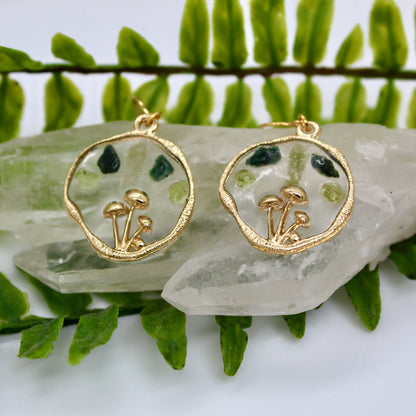 Gold mushroom earrings with peridot and moss agate gemstone displayed on crystal