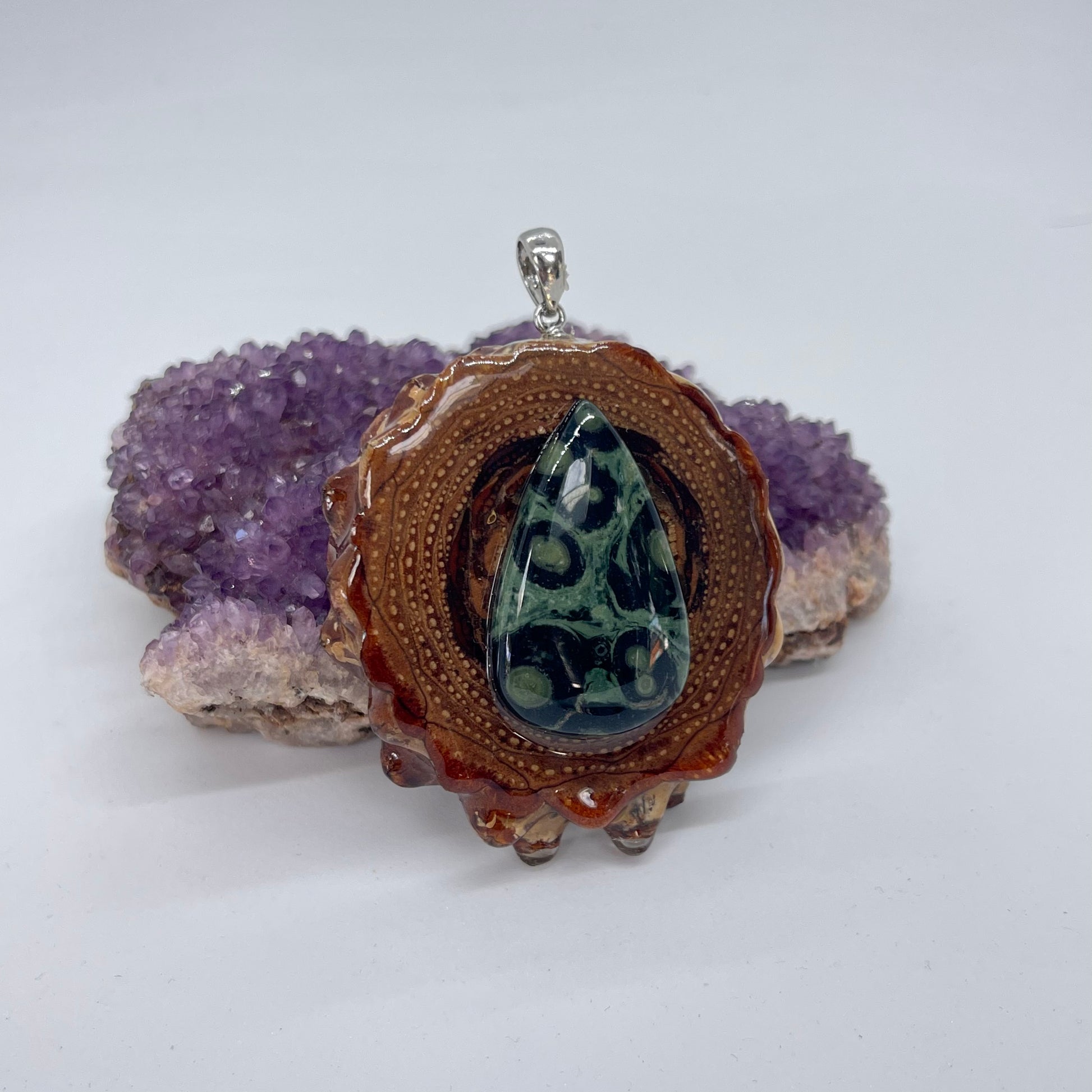 sideview of kambaba jasper stone on pinecone pendant displayed on crystal with white background
