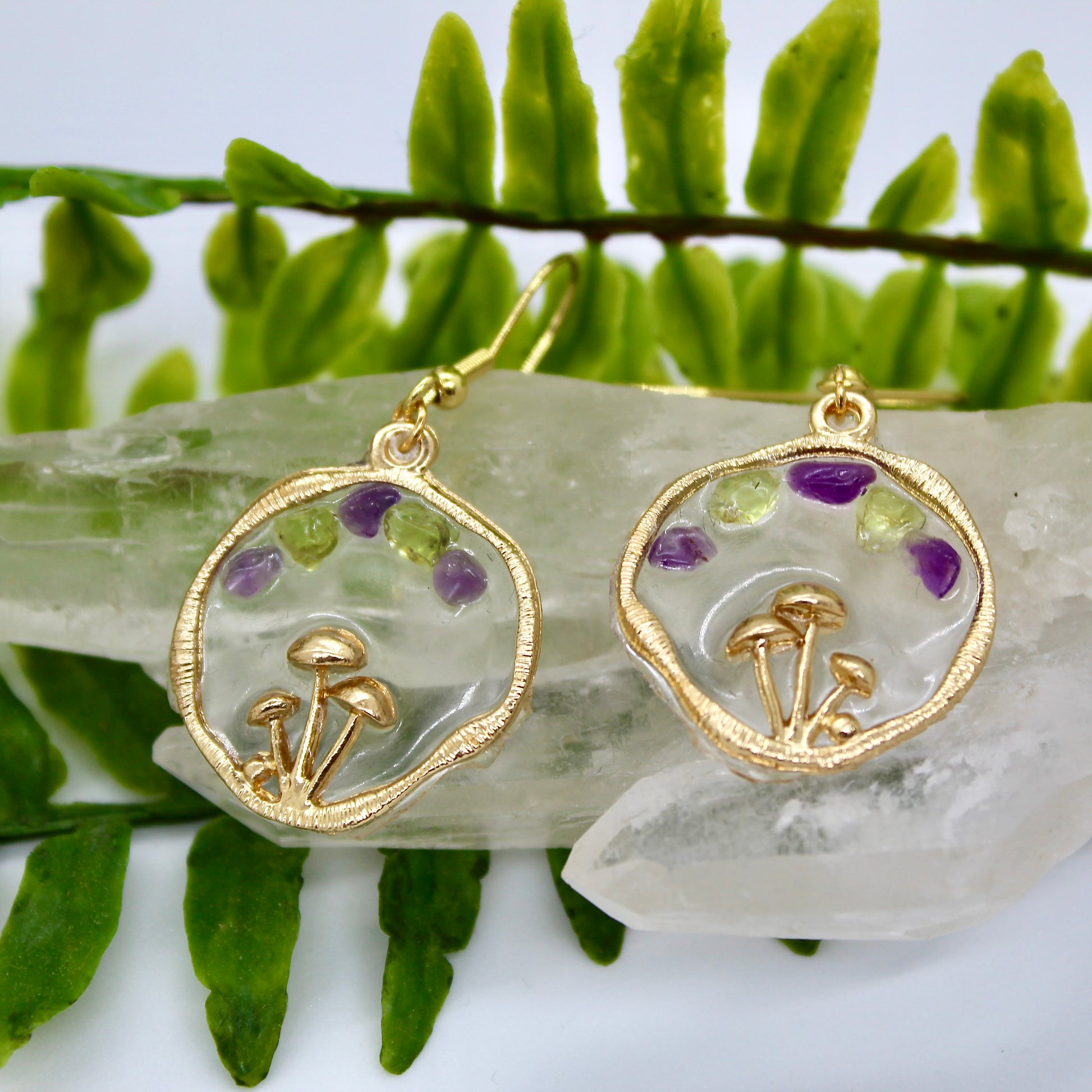 gold mushroom earrings with purple and green gemstones displayed on crystal 