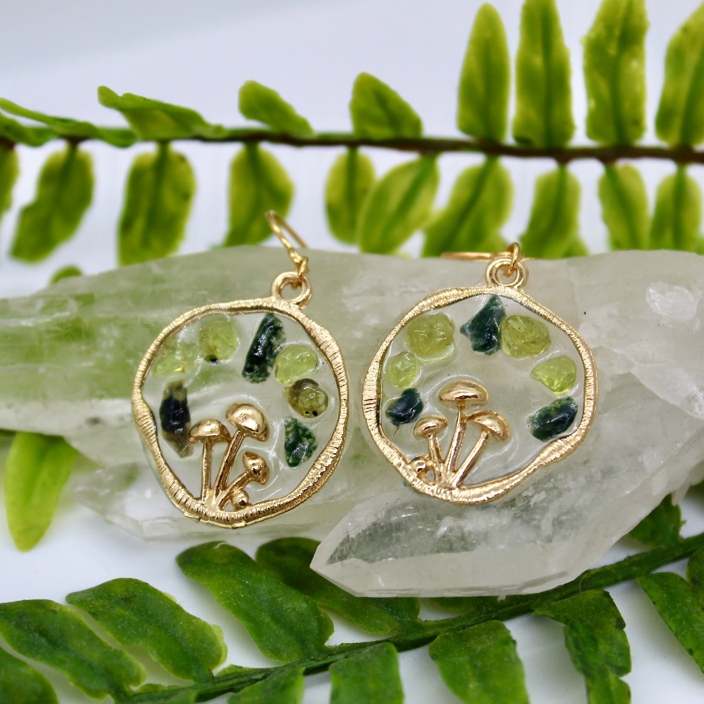 peridot and moss agate gold mushroom earrings displayed on crystal with plant background 