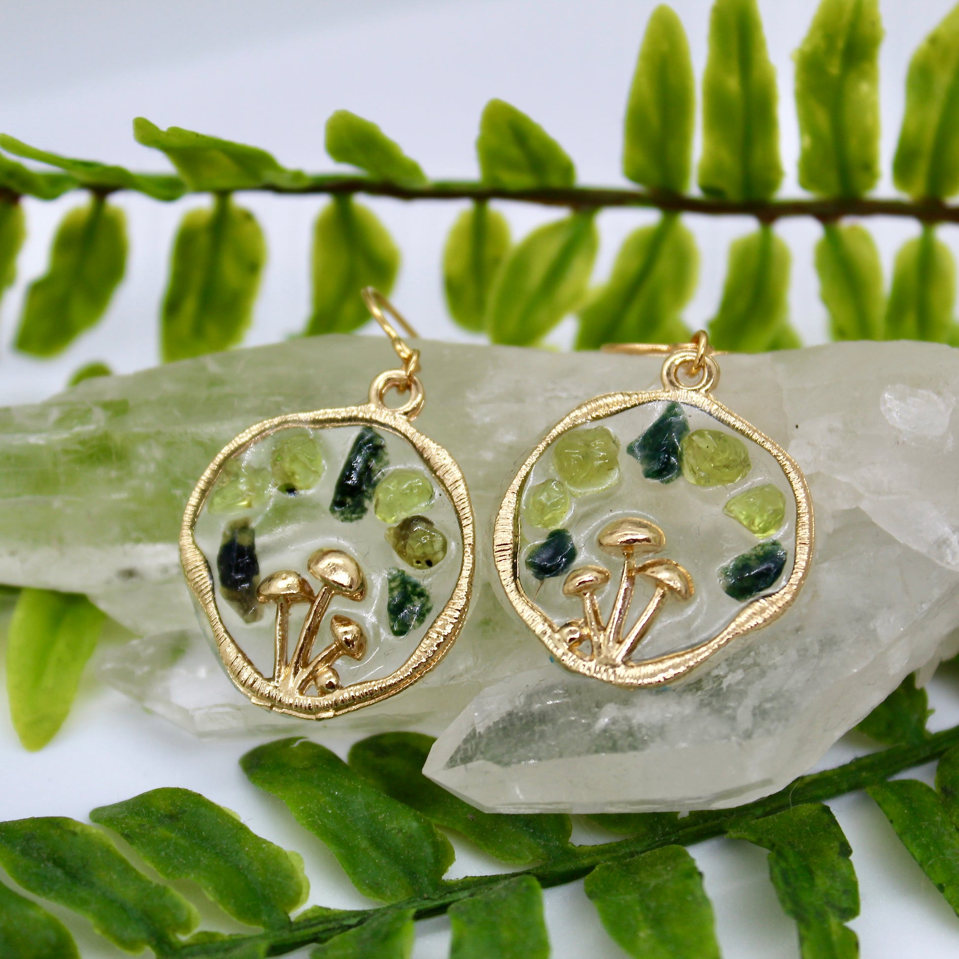 peridot and moss agate gold mushroom earrings displayed on crystal with plant background 