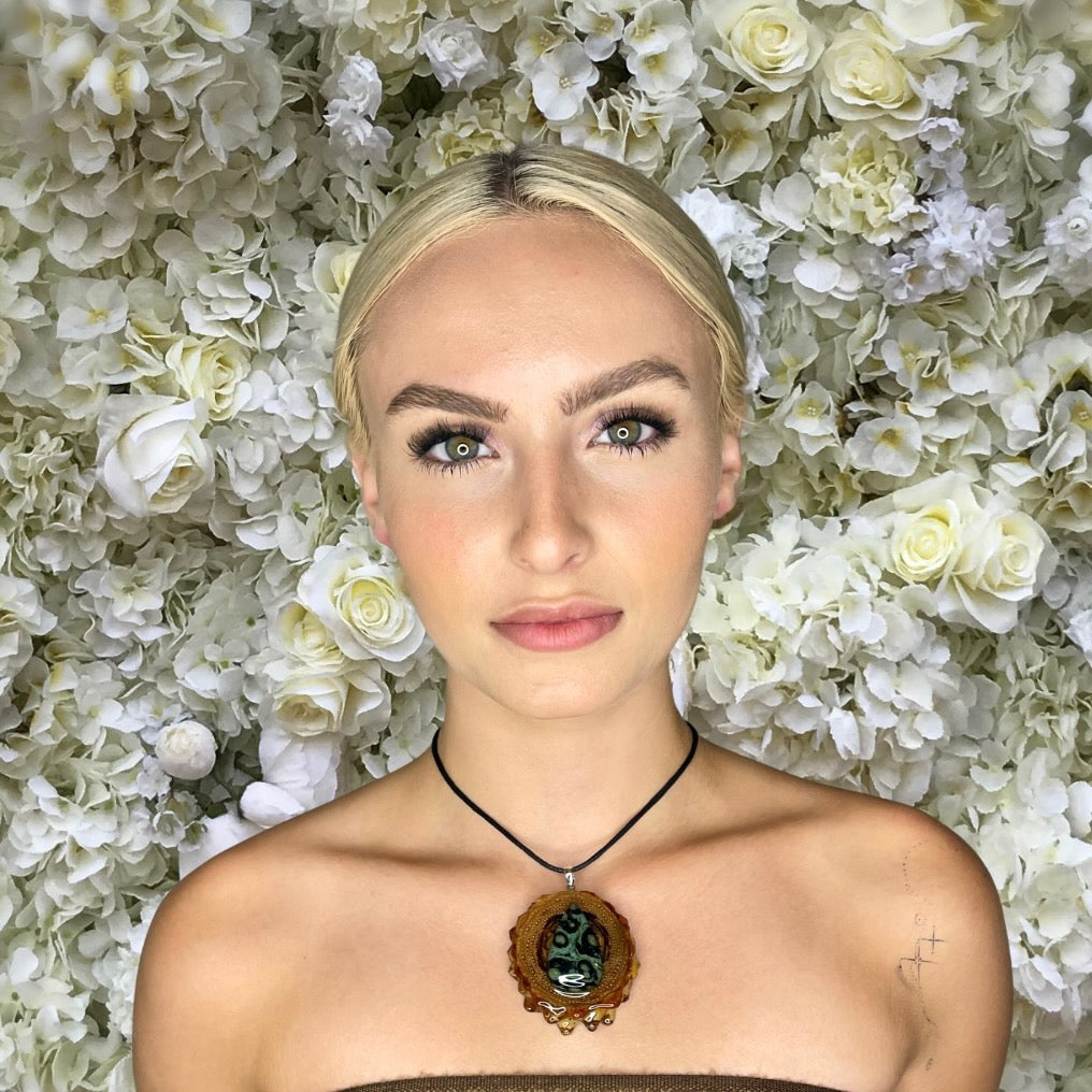 model wearing pinecone pendant with Kambaba jasper stone in front of flower background